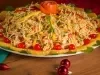 Em cima de uma mesa, prato de salpição colorido com frango desfiado, pimentões em tiras, milho-verde e batata-palha, decorado com laranja em rodelas, tomates e no topo do prato fio de cenoura em forma de flor.