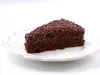 Imagem de uma fatia de bolo de chocolate com recheio e cobertura de brigadeiro e chocolate granulado sobre um prato branco.