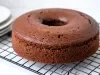Em cima de uma mesa,  grade com bolo com furo no meio de chocolate fofinho.