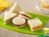 Sanduiches variados de pão branco com recheios coloridos, em formatos redondo, triangular e quadrado.