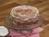 Foto aproximada da receita de Bolo de Baba de Moça com Nozes, decorado com fitas de coco, sobre um prato de vidro em cima de um pano cor de rosa, numa bancada de madeira com um pedaço de coco.
