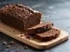 Bolo de chocolate recém-assado em uma tábua clara, coberto com gotas de chocolate. Duas fatias cortadas mostram a textura úmida. A apresentação casual é realçada por migalhas e um fundo escuro, destacando o bolo apetitoso.