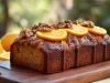 Fotografia de um bolo de laranja com nozes, exibido em uma tábua de madeira. O bolo tem uma crosta dourada e é decorado com fatias de laranja e metades de nozes.