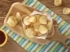 Imagem vista de cima de chips de batata-doce sobre uma tábua de madeira com um potinho amarelo com ketchup ao lado.