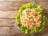Fotografia de salpicão em um prato redondo de madeira, com alface crocante, cenouras, milho-verde, azeitonas, pedaços de frango e batata palha, dispostos de forma atraente sobre um pano xadrez.