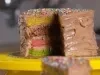 Fotografia em tons claros de um bolo inteiro sobre um apoio de bolo amarelo. O bolo está sem uma fatia, mostrando as camadas coloridas.
