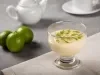 Fotografia em tons de branco com uma taça de sobremesa de vidro ao centro dentro da taça existe uma receita de mousse de limão coberta com raspas de limão.