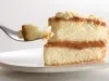 Fotografia de uma fatia de bolo bem-casado com doce de leite sobre um prato raso branco apoiado em uma mesa branca.