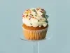 Imagem de um cupcake em forma branca decorado com chantily branco e granulados coloridos.
