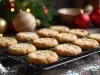 Em cima de uma mesa decorada com enfeites de natal, em cima de uma grade há biscoitos crocantes polvilhado com açúcar de confeiteiro.