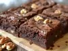 Imagem de quatro pedaços quadrados de brownie com nozes um ao lado do outro sobre uma tábua de madeira.