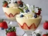 Taça com creme branco cremoso e morangos cortados ao meio. Decorado com flores comestíveis, morango e uvas roxas.