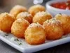 Em cima de uma mesa, prato branco com bolinhos crocantes e dourados, polvilhados com queijo ralado.
