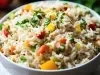 Em cima de uma mesa, tigela redonda com porção de arroz soltinho com pimentões amarelo, vermelho, ervilhas e cenouras picadas.