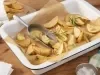 Fotografia em tons de amarelo e verde em uma bancada de madeira clara, um recipiente retangular com batatas feitas no forno e ramos de alecrim em cima dela. Ao lado, um pano xadrez em amarelo e verde.