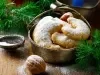 Em cima de uma mesa decorada com enfeites de natal, recipiente com biscoitos em forma de meia lua, polvilhados com açúcar de confeiteiro.