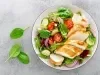 Fotografia de um peito de frango grelhado e fatiado servido em cima de uma salada de folhas e tomates