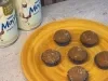 Seis brigadeiros caramelizados em forminhas azuis sobre prato amarelo, com latas de LEITE MOÇA® ao fundo.