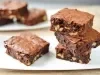 Imagem de três pedaços quadrados de brownie empilhados e um pedaço ao lado.