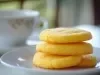 Em cima de uma mesa, prato branco redondo com biscoitos dourados e crocantes enfileirados.