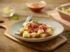 Imagem de um prato rústico com nhoque de batata com molho de tomate decorado com uma folha de manjericão.