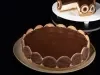 Em cima de uma mesa, prato redondo com torta de biscoitos calipso, com ganache de chocolate.