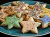 Em cima de uma mesa, prato redondo com biscoitos em formato de estrelas de Natal, decorados com glacê e confeitos de bolinhas coloridas.