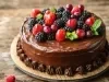 Um bolo de chocolate coberto com um brilho de chocolate, decorado com morangos, amoras e uvas vermelhas. A apresentação é elegante, com detalhes em chocolate ao redor da base, tudo sobre uma superfície de madeira rústica.