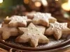 Em cima de uma mesa, biscoitos de estrelas, decorados com confeito prata de bolinha.