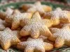 Em cima de uma mesa, prato com biscoitos em formato de estrelas, polvilhado com açúcar de confeiteiro.
