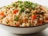Prato de porcelana branco com arroz soltinho, cenouras cortadas em cubos, ervilhas, decorado com pedaços de salsinha.