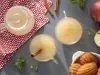 Imagem vista de cima de duas xícaras de chá de maçã, decorado com um pedaço de canela, maçãs e um pote de madeleines