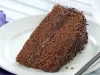 Foto de um prato branco numa mesa de madeira branca com uma fatia de bolo de chocolate dentro e um garfo do lado