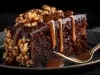 Fatia de bolo de chocolate úmida, coberta com ganache brilhante e um fio de caramelo. Decorada com nozes picadas, com um garfo dourado ao lado, destacando a delícia do doce.