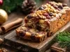 Fotografia de um bolo de frutas festivo, exibido em uma tábua de madeira rústica, repleto de frutas secas e nozes, cercado por elementos natalinos como ramos de pinheiro e canela.
