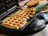 Imagem de uma máquina para waffles com waffles quadrados e uma espátula verde.