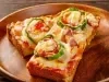 Fotografia de um pão pizza de queijo deretido com tomate, cortado na metade e a outra metade esta apoiado sobre a outra metade. As metades estão em um prato redondo de madeira raso.