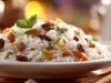 Prato de arroz branco, soltinho, com uma textura leve e fofa com uvas-passas pretas, decorado com folha de coentro.
