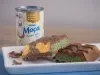 Barra de Dubai, receita de uma barra de chocolate recheada com um creme de pistache e macarrão, decorada com pó dourado e servida em um prato branco ao lado de uma lata de Leite Moça