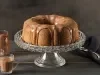 Imagem de um bolo formigueiro inteiro redondo com furo central coberto de calda de chocolate sobre uma boleira transparente