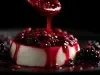 Fotografia em tons escuros de uma sobremesa com mousse com uma calda de frutas vermelhas sobre e ao redor da mousse, sobre um prato raso preto. Tem um pouco de calda caindo na mousse de uma colher de sopa.