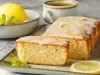 Imagem de um prato retangular com um bolo de limão com cobertura e raspas com uma fatia em destaque. Ao lado limões e rodelas de limão.