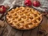 Imagem de uma torta de maçã trançada bem dourada com maçãs ao redor.