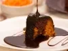 Um pedaço de bolo de cenoura com calda de chocolate escorrendo por cima. A cobertura está sendo servida no momento, o que dá um visual ainda mais apetitoso ao bolo. O interior do bolo parece úmido e bem estruturado.