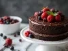 Um bolo de chocolate de duas camadas, coberto com ganache brilhante e decorado com uma variedade de frutas vermelhas, como morangos, framboesas e mirtilos.