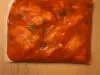 Fotografia de um frango dentro de um saco plástico imerso em um molho de tomate e manjericão