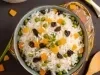 Imagem de cima de uma tigela com arroz colorido com passas, ervilhas e cenouras picadas.