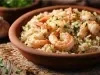 Em cima de uma mesa, prato de porcelana redondo com arroz branco soltinho e camarões, decorado com cheiro-verde.
