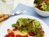 Fotografia em tons de azul em uma bancada de madeira clara, um pano azul, um prato branco redondo raso com o frango à parmegiana e uma salada verde em cima dele. Ao lado, talher, um copo com água e rodelas de limão e um potinho com mais salada.