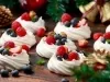 Imagem de mini pavlovas de iogurte decoradas com frutas vermelhas sobre uma mesa de madeira e decoração de Natal.